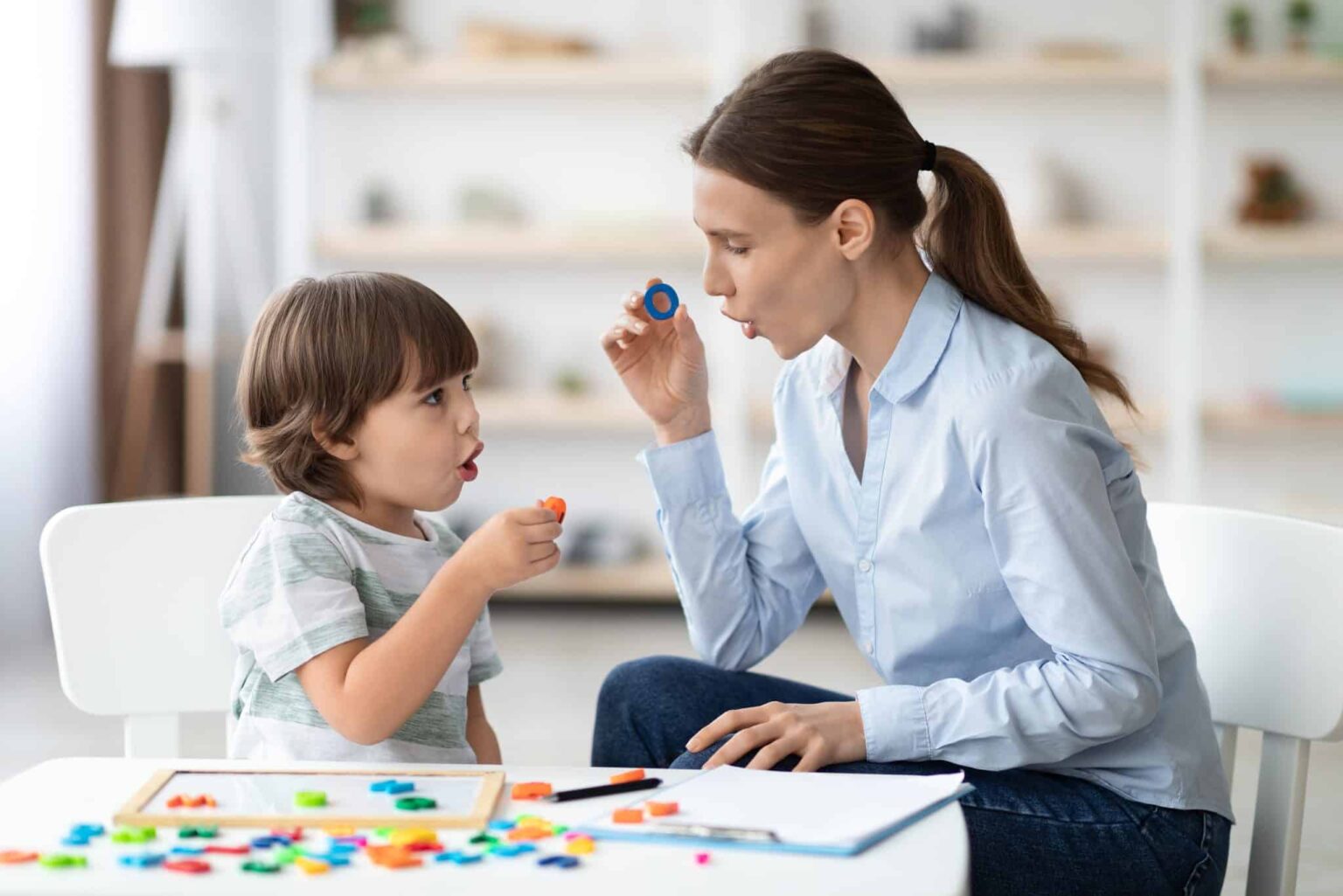 Auditory-Verbal-Therapy-session Speech therapist with a small child. They are both holding the letter O and making the sound that it makes together.