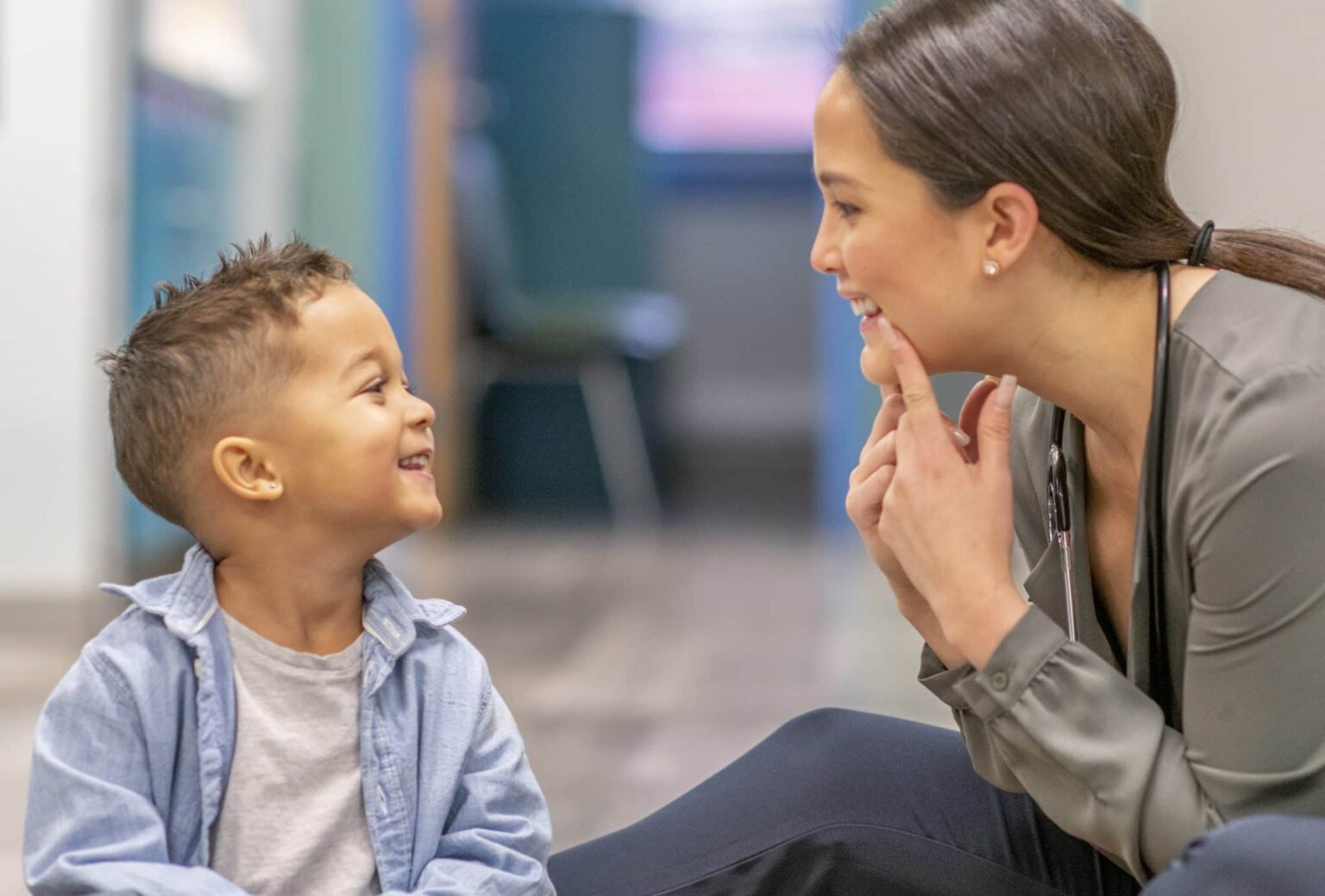 Speech therapy session A small child is smiling up at a medical practitioner who is making a funny face at him and holding the corners of her mouth up while smiling.